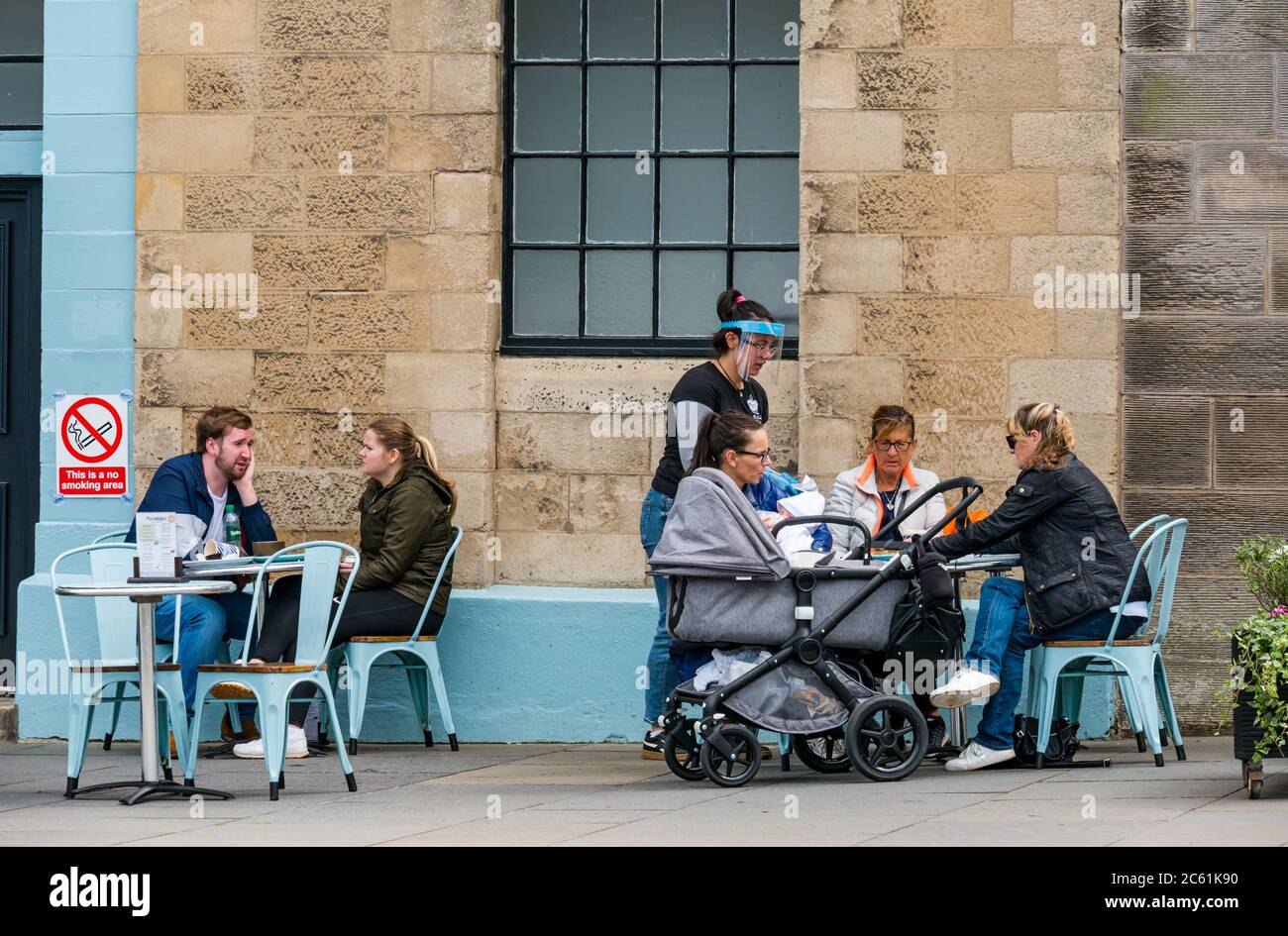 Leith, Edinburgh, Scotland, United Kingdom, 6th July 2020. Cafe culture & pub opening begin: cafes and pubs along The Shore are beginning to offer pavement spaces for meals and drinks and the area feels much busier than in recent months. Pub beer gardens and outdoor spaces can open from today in Scotland. Customers sitting outside at Mimi's Bakehouseare served by a waitress wearing a visor Stock Photo