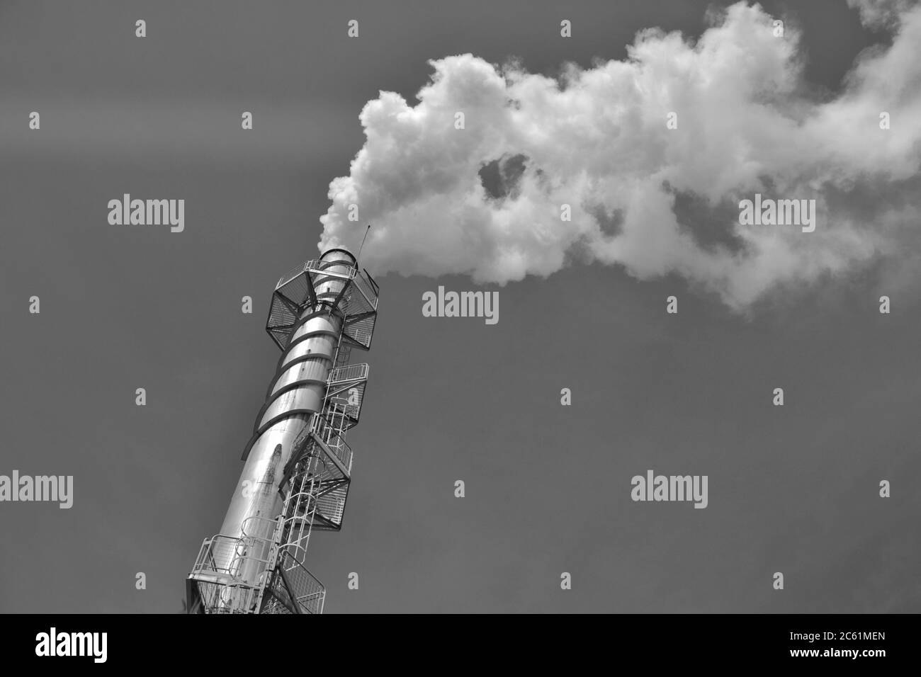 Chimney in an industrial district of a city in the interior of Brazil, releasing white smoke, blue sky background, black and white photography Stock Photo