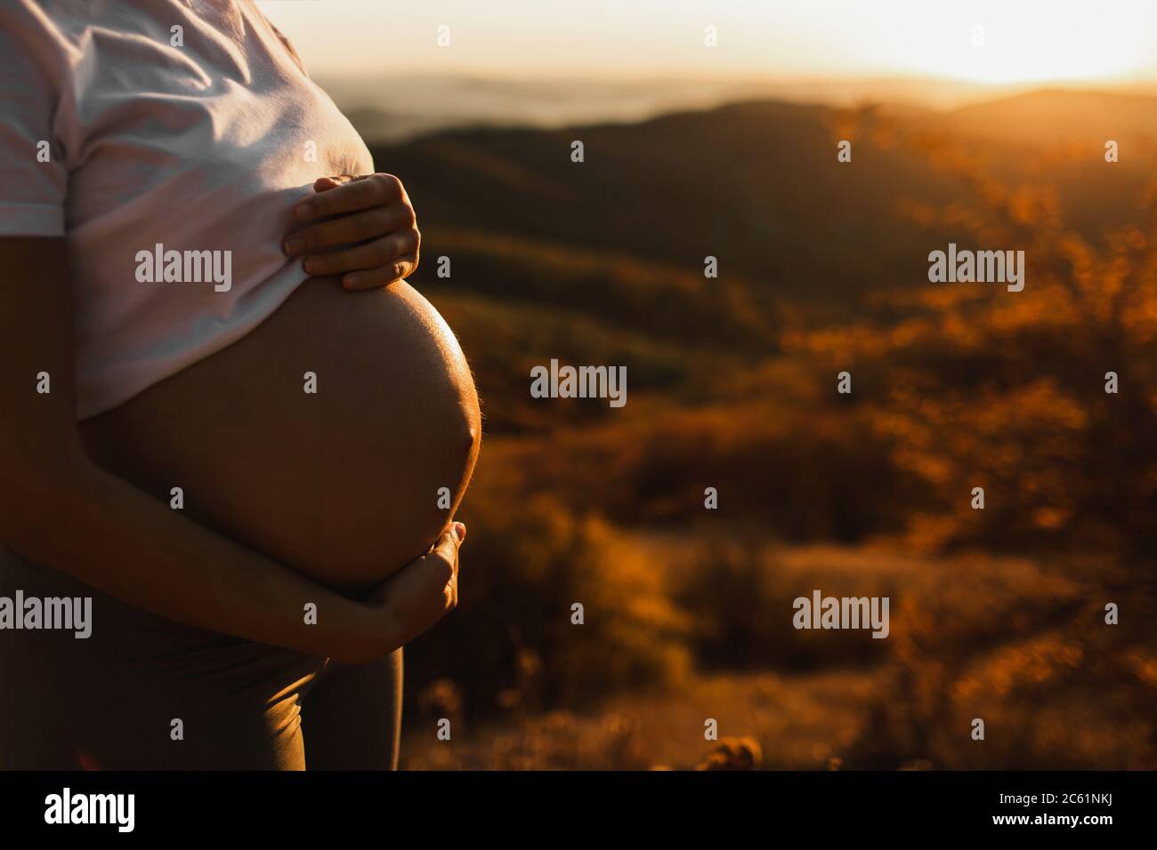 Woman hands hold belly in pregnancy outdoors closeup. Amazing warm sunset light. Maternity and childbirth concept. Stock Photo
