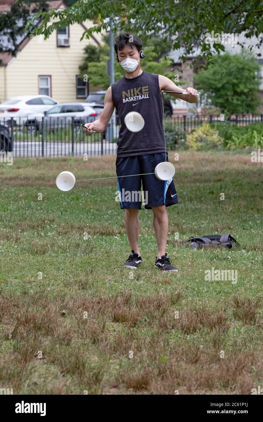 An Asian American man wearing a surgical mask performs on a Chinese yoyo called Diablo. In Kissena Park, Flushing, New York City. Stock Photo