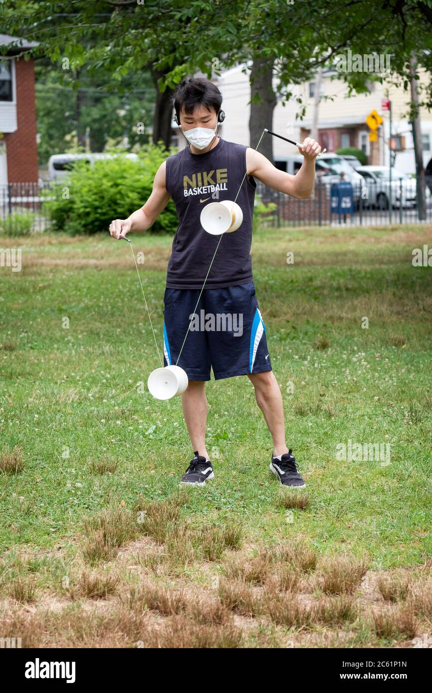 An Asian American man wearing a surgical mask performs on a Chinese yoyo called Diablo. In Kissena Park, Flushing, New York City. Stock Photo