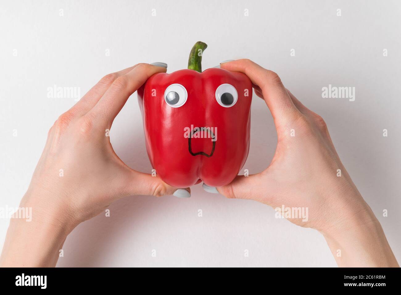 Hands holding large red pepper with funny scared face. Pepper with ...