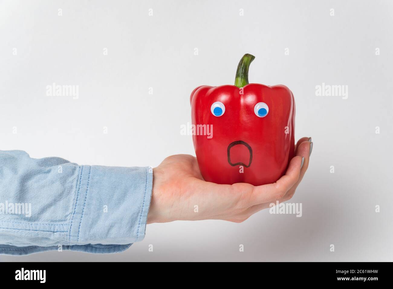 Large red bell pepper, Googly eyes on palm. Scared pepper character. White background Stock