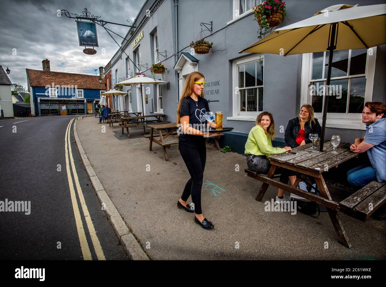 Thaxted, UK. 06th July, 2020. Thaxted Essex UK. Swan Pub re opens after Covid-19 three month Coronavirus lockdown. 6 July 2020 Staff wearing personal protective equipment (PPE) visor as they serve drinks to customers seated outside the front of the pub at The Bullring in the medieval town of Thaxted in north Essex, England. Customers order their drinks after giving mobile/cell phone numbers and names in if they need to be contacted in case of a local Covid-19 outbreak. Credit: BRIAN HARRIS/Alamy Live News Stock Photo