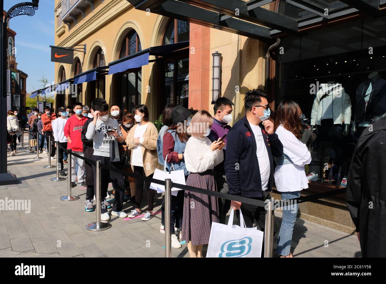 Crowd of people wearing protective mask to prevent coronavirus, queue up outside NIKE store, waiting for shopping. Stock Photo