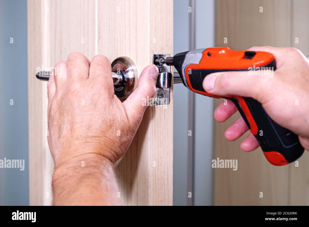 Repair of the door handle. The master clamps the loose screw with an electric screwdriver Stock Photo