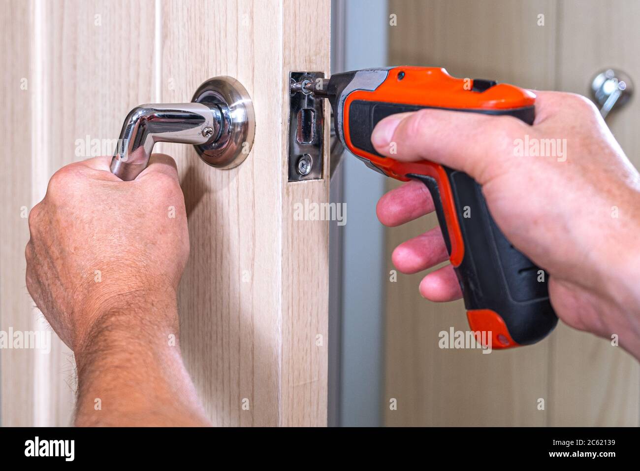 Repair of the door handle. The master clamps the loose screw with an electric screwdriver Stock Photo