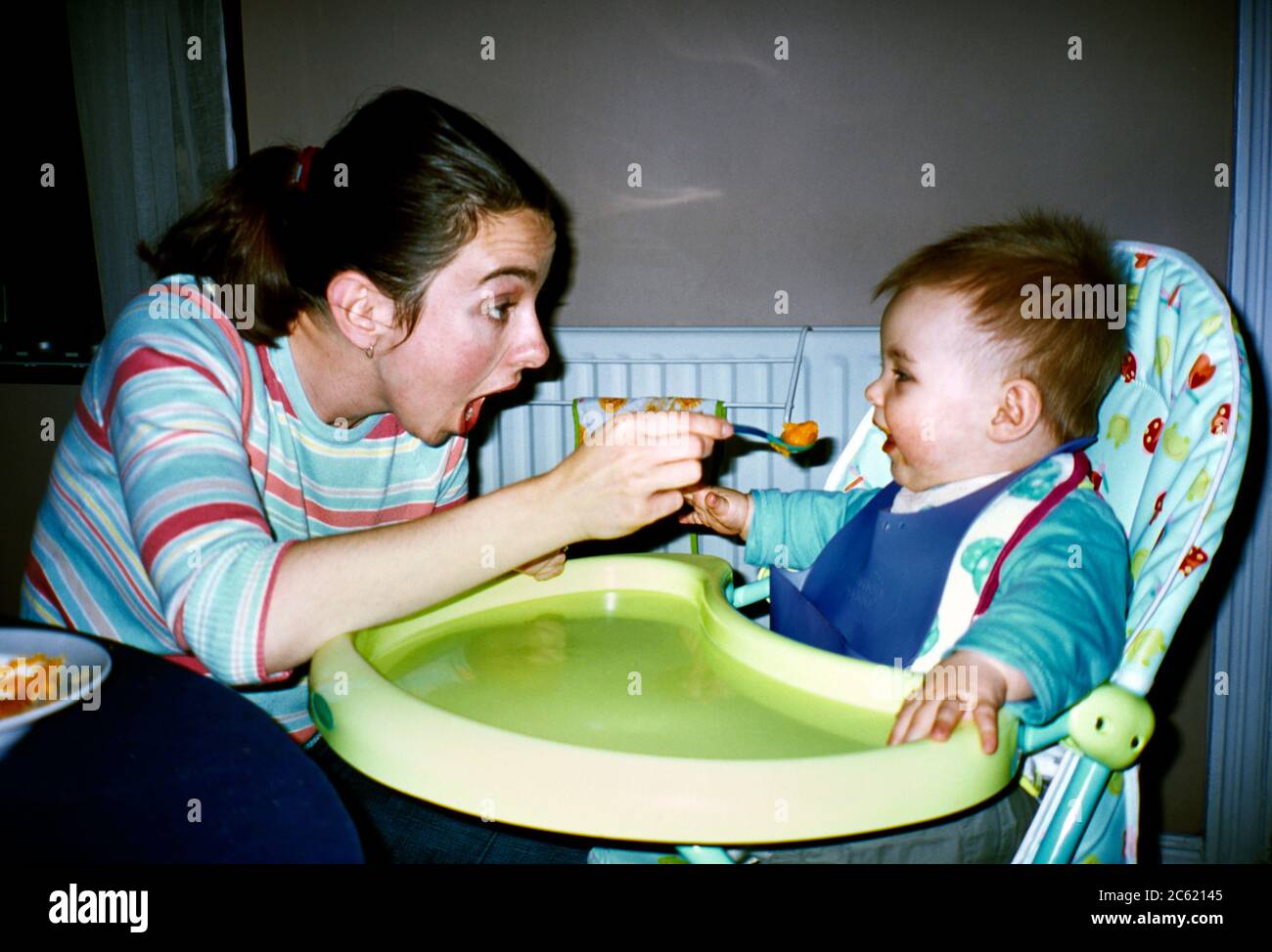 Mother Feeding Seven Month old Baby Boy Sitting in high Chair Stock