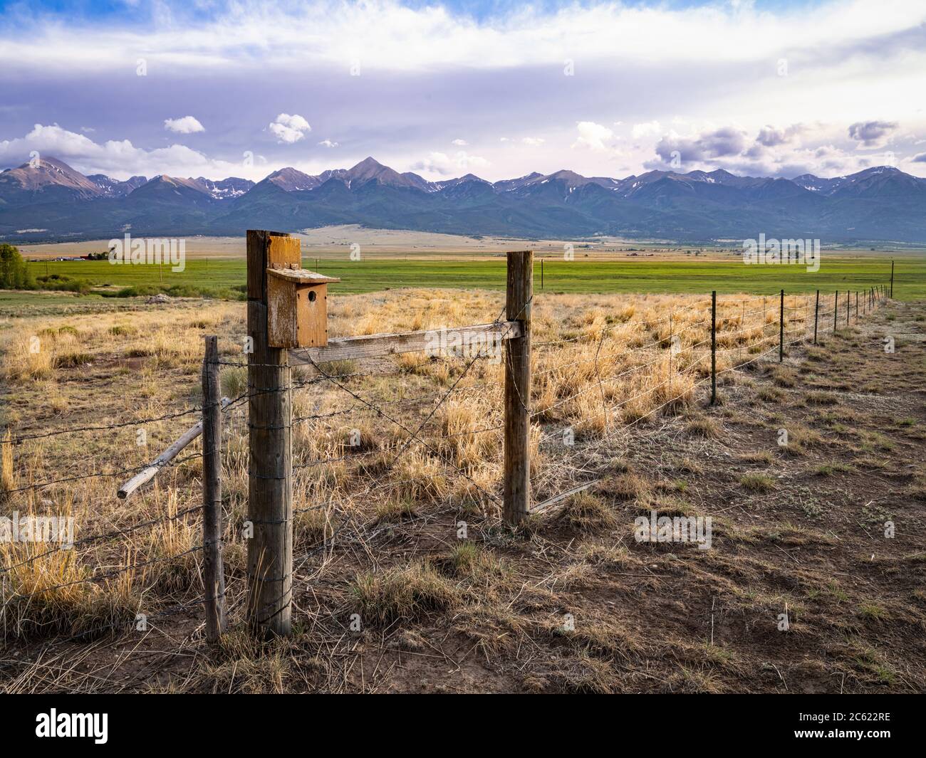 Bird house on post of barbed wire fence, with mountains. Colorado, USA Stock Photo