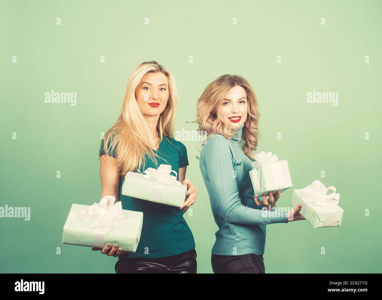 Fashion lifestyle portrait of two girls friends holding birthday bright presents, wearing trendy clothes. Going crazy and making funny faces. Stock Photo