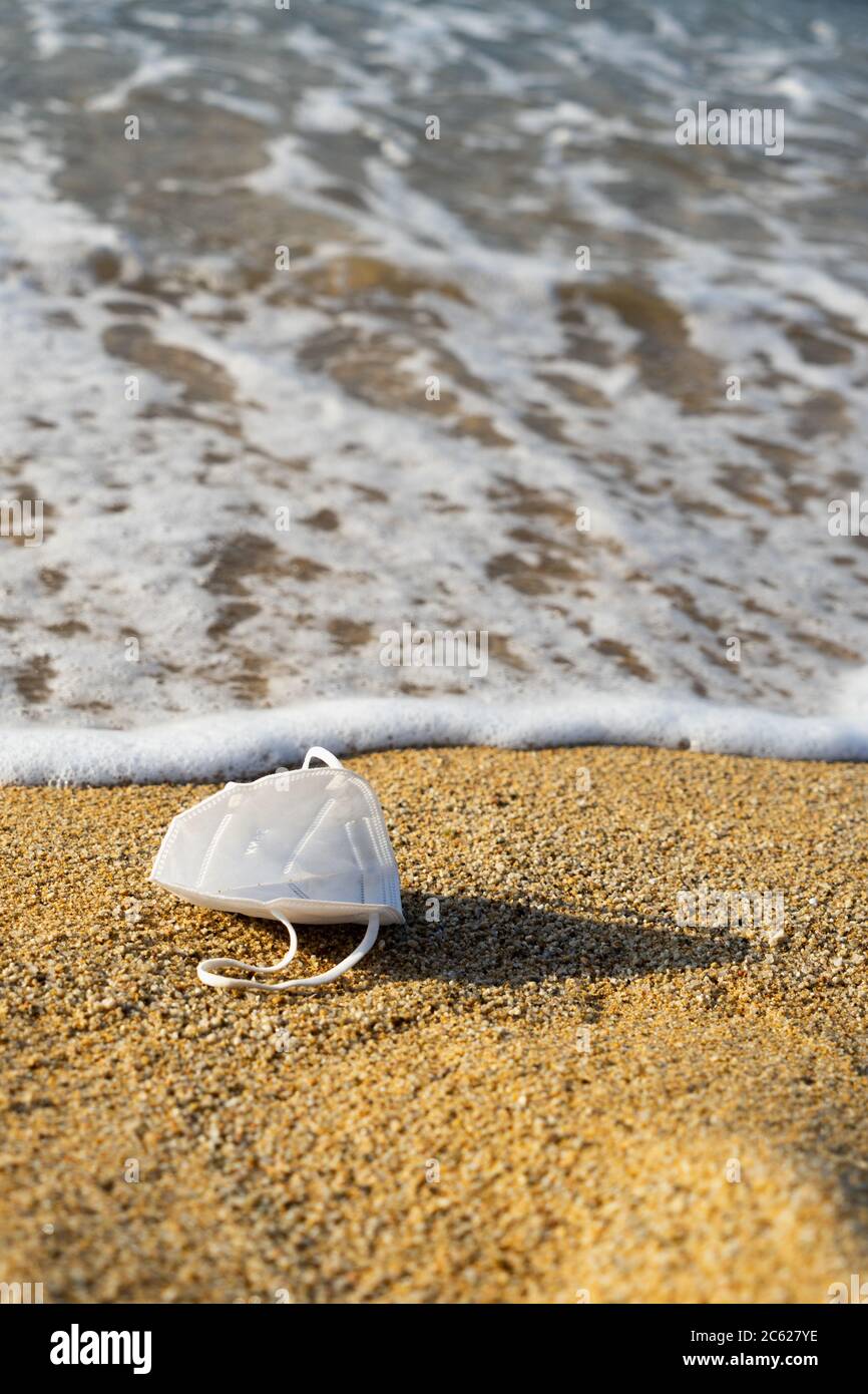 Covid-19 coronavirus mask used and thrown at the seashore. Responsibility, contagion, cleaning and garbage concept. Stock Photo