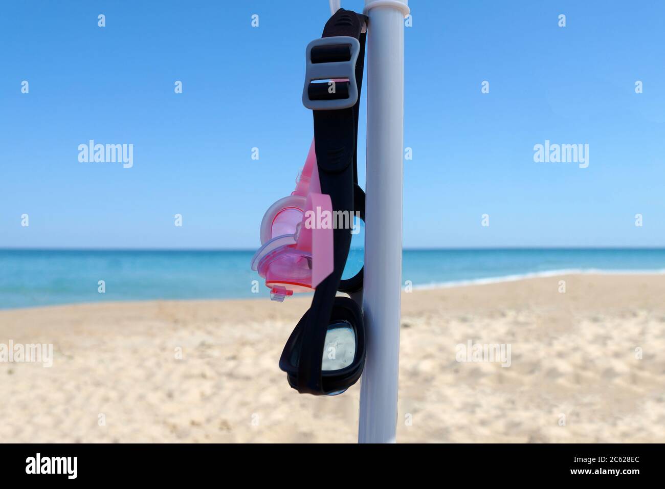 two pairs of swimming goggles hang under a beach umbrella on a sunny