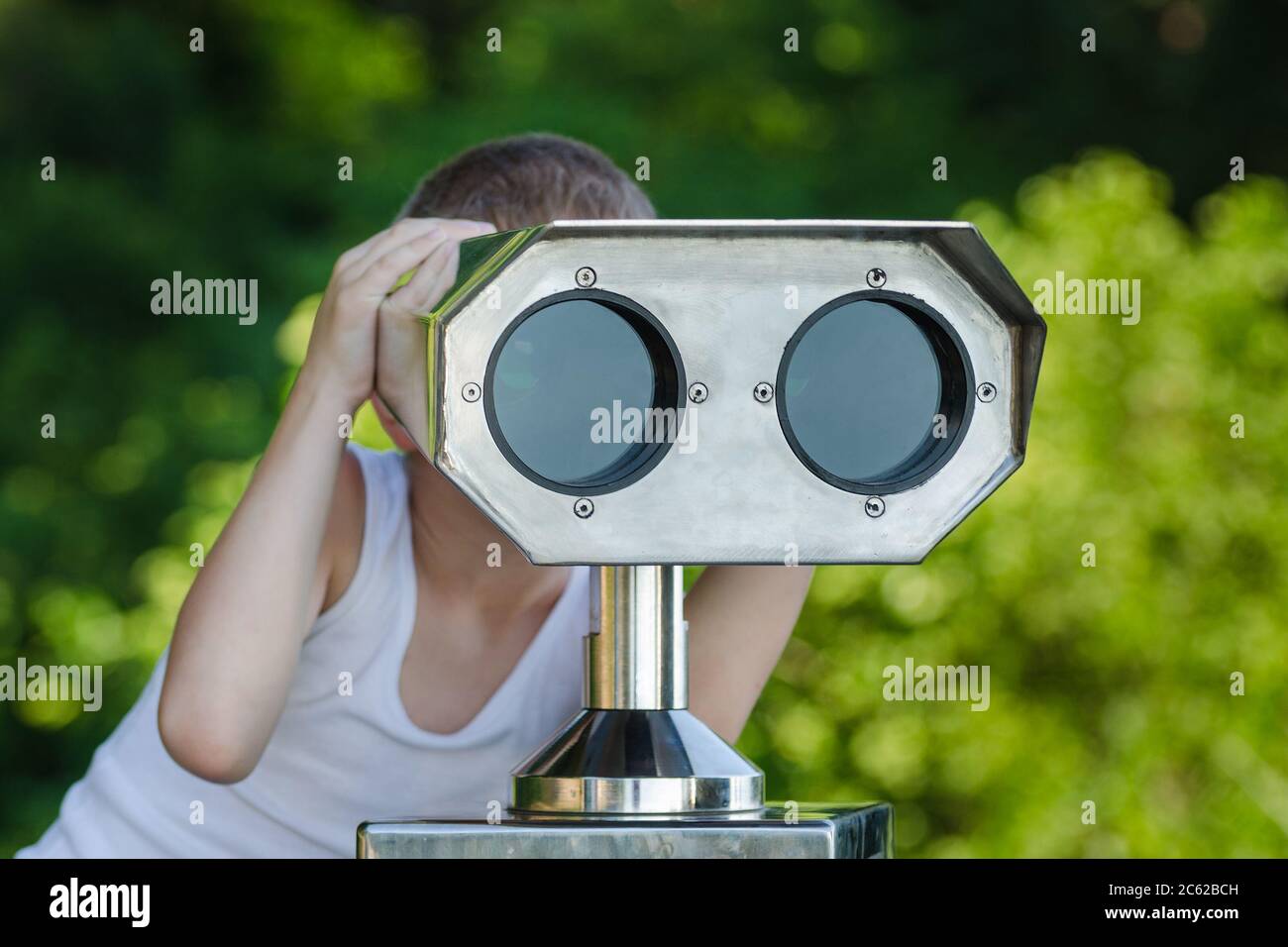 Boy looking through a tourist telescope on green Park background Stock Photo