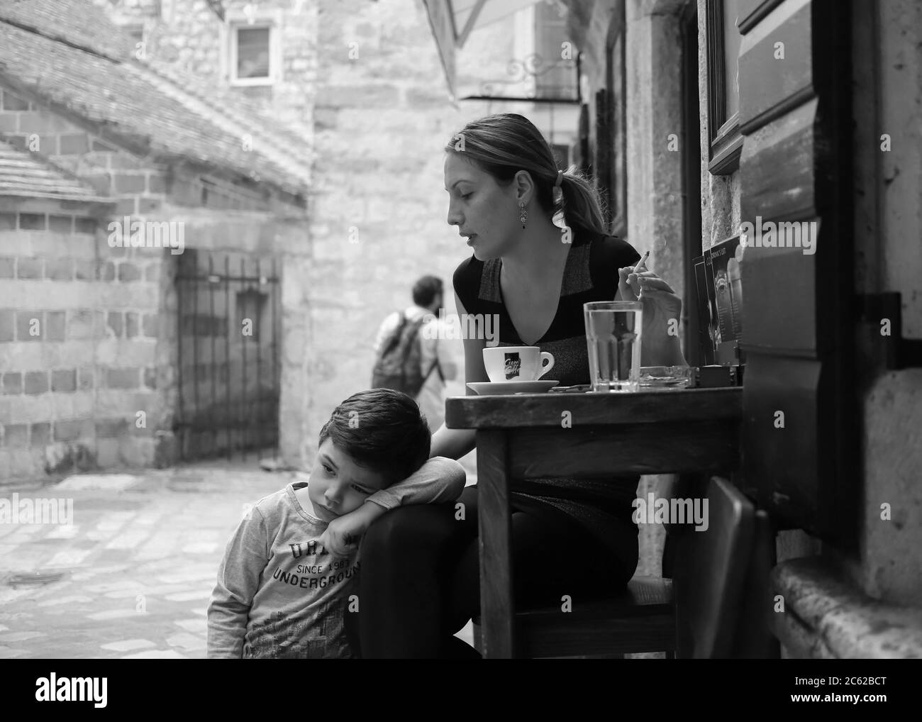 Montenegro, Sep 22, 2019: Sleepy boy and his mother spend time at a street café in Kotor Old Town (B/W) Stock Photo