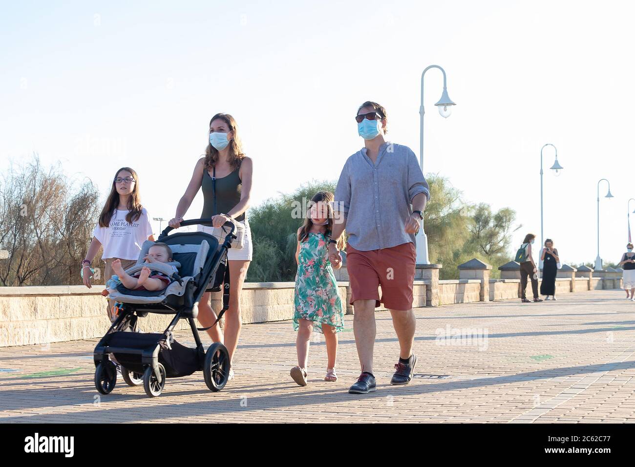 Huelva, Spain - June 3, 2020: Family walking by Islantilla promenade wearing protective mask due to covid-19. Stock Photo