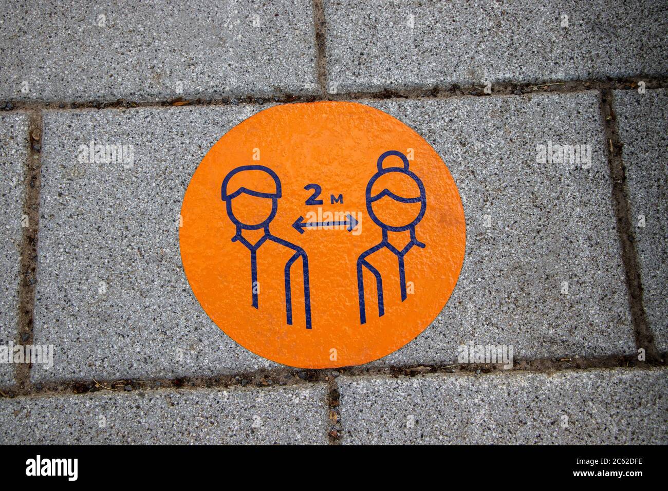 Orange circle decal marker 2m social distance on a commercial street on the ground sidewalk for passerby during COVID-19 Coronavirus Pandemic; Stock Photo