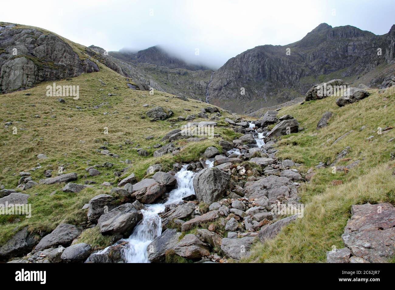 Mountain stream leads up towards Clogwyn with Snowdon shrouded in cloud, Snowdonia National Park, North Wales Stock Photo