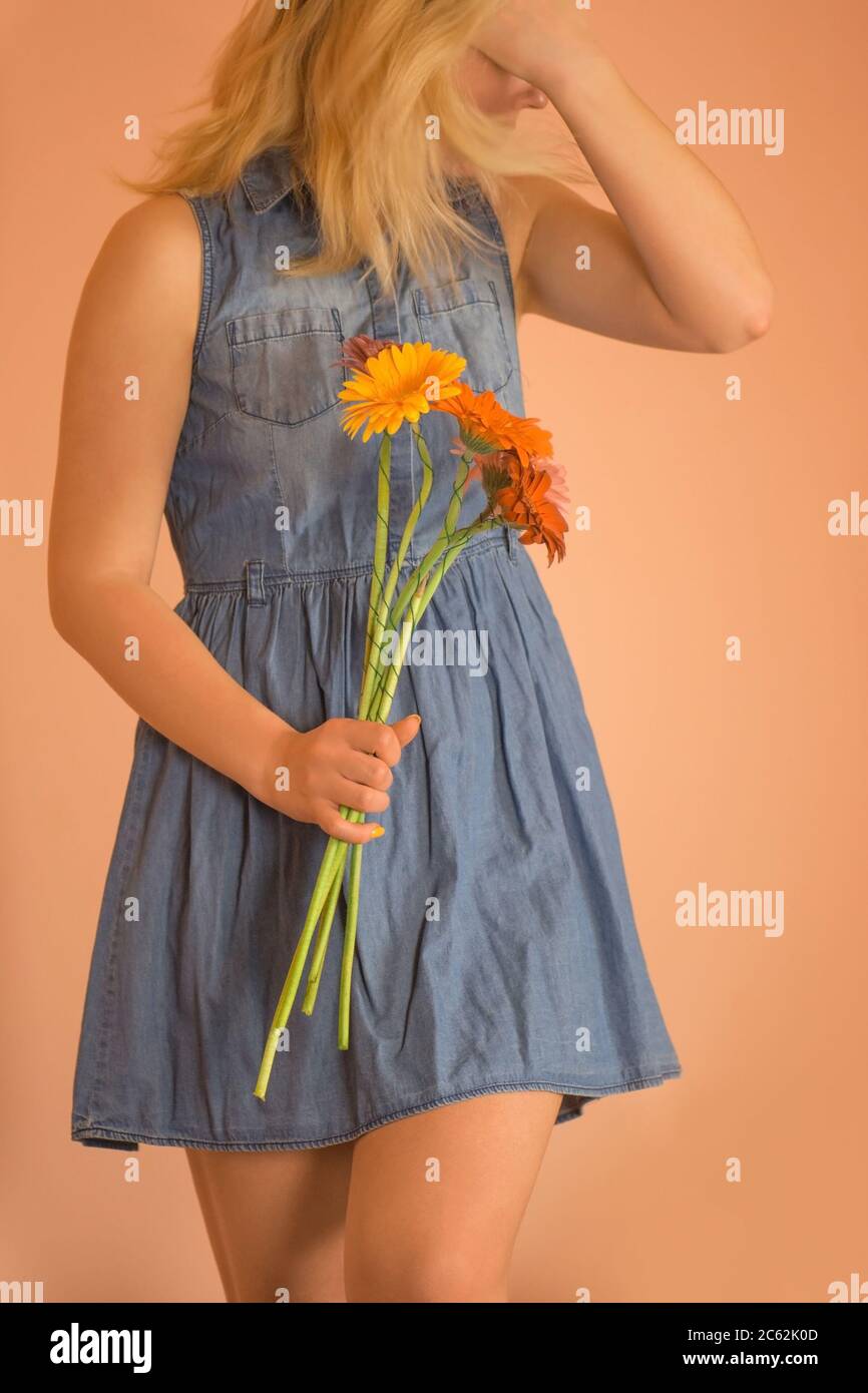 Blonde girl wearing denim dress holding chamomile bouquet. Stock Photo
