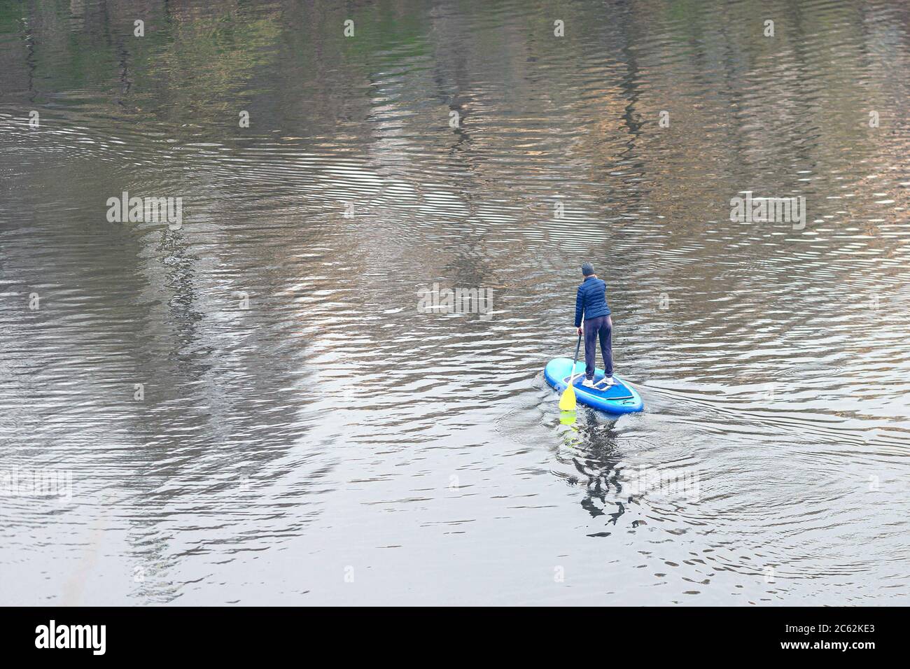 Top view of trained woman standing on the stand-up paddle board and walking on the calm water of river. Girl paddling on SUP in river. Stock Photo