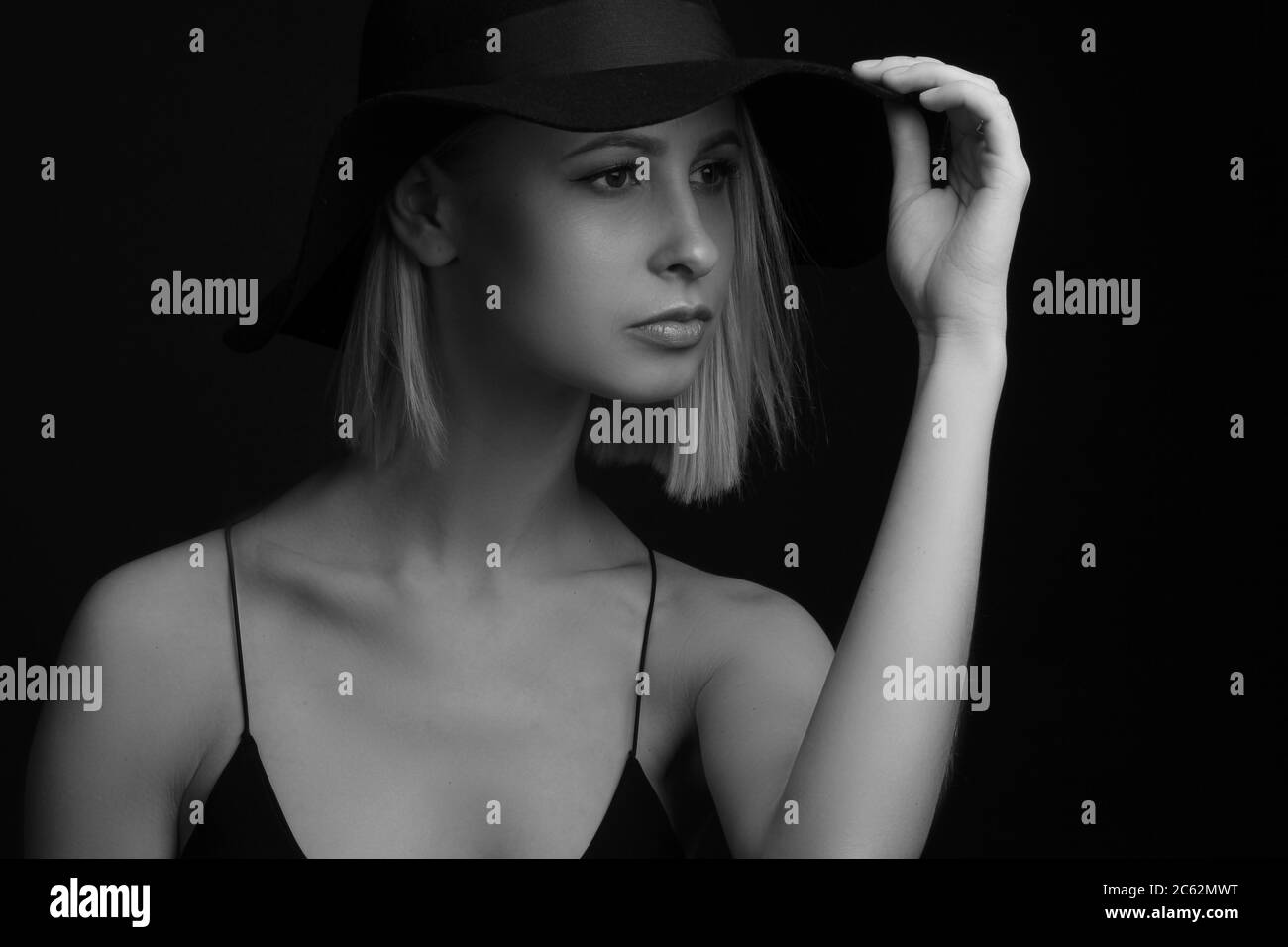 Black and white portrait blondes on a black background in a hat and Tank Top With Thin Straps. holding the brim of his hat with his hands Stock Photo