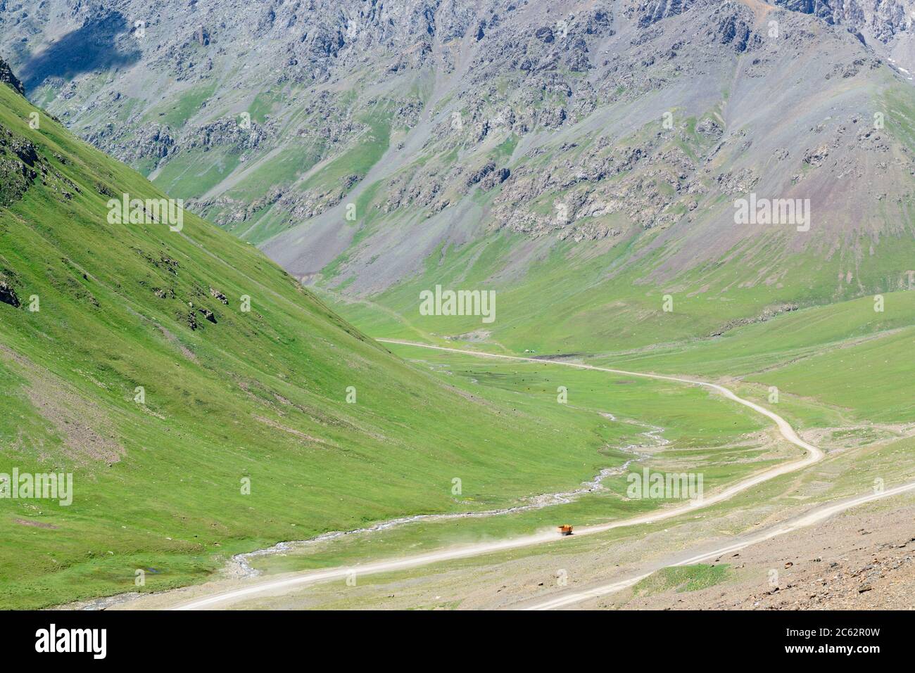 Orange truck driving in a valley in the Tian Shan mountains of Kyrgyzstan Stock Photo