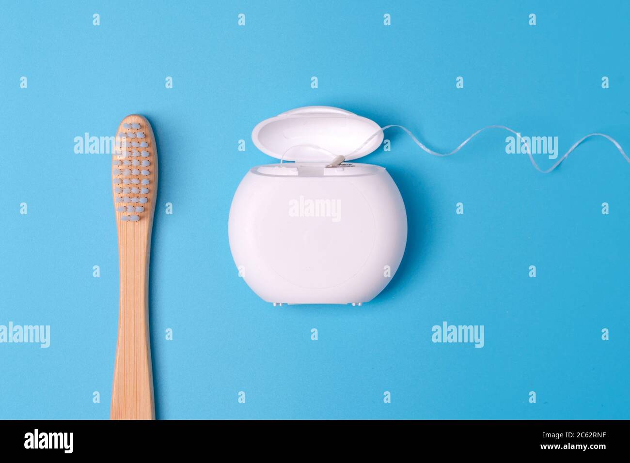 Dental floss container and bamboo toothbrush on blue background. Daily