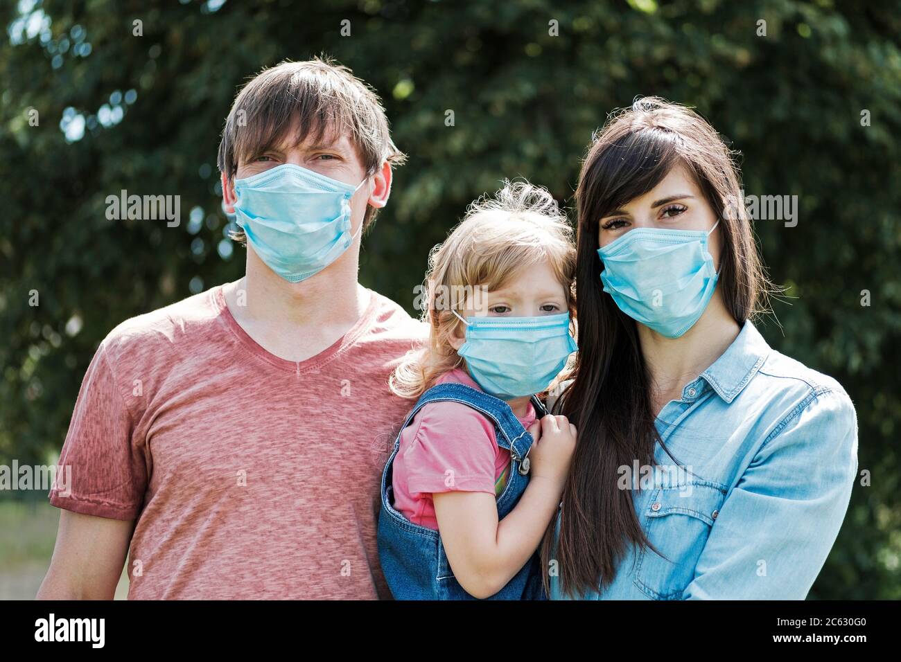Young family with daughter wearing protective surgical face masks during the Covid-19 or coronavirus pandemic Stock Photo