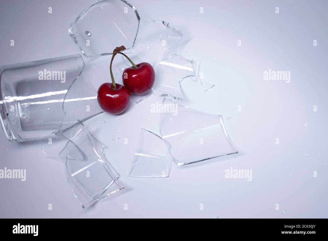 pieces of broken glass are scattered on a gray-white background with a cherry on it. High quality photo Stock Photo