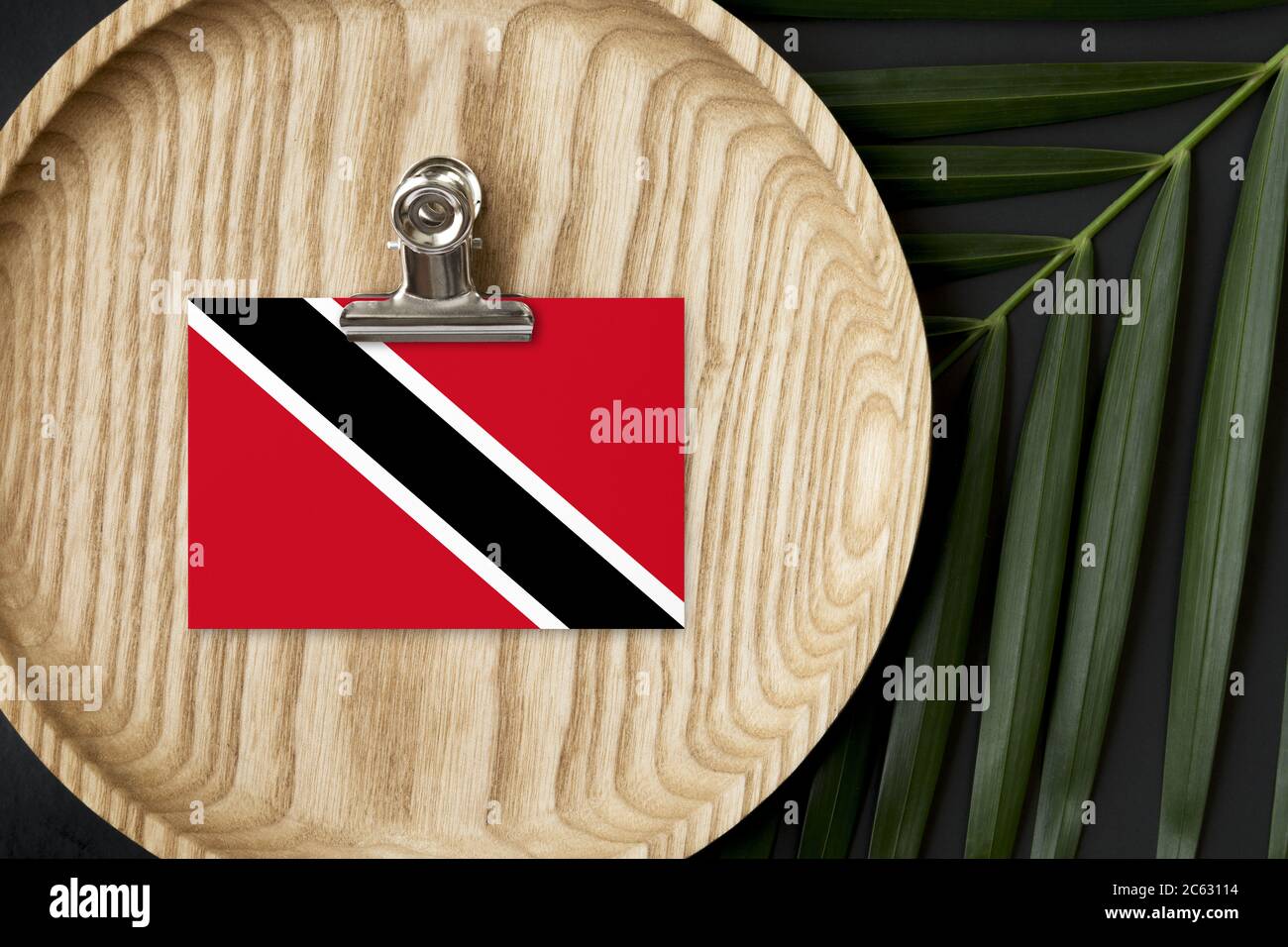 Trinidad And Tobago flag tagged on wooden plate. Tropical palm leaves monstera on background. Minimal national concept. Stock Photo