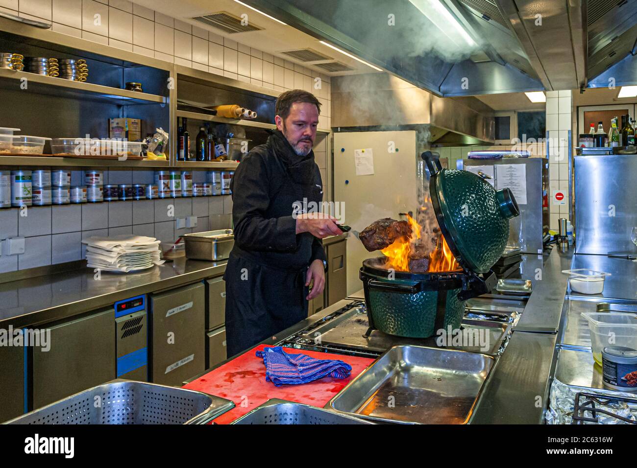 German 3 Michelin star chef Marco Müller with Big Green Egg. One of the secrets of tender beef brisket is the "reverse" order: first heat it in the oven at low heat and then grill it hot in its own smoke just before cutting it Stock Photo