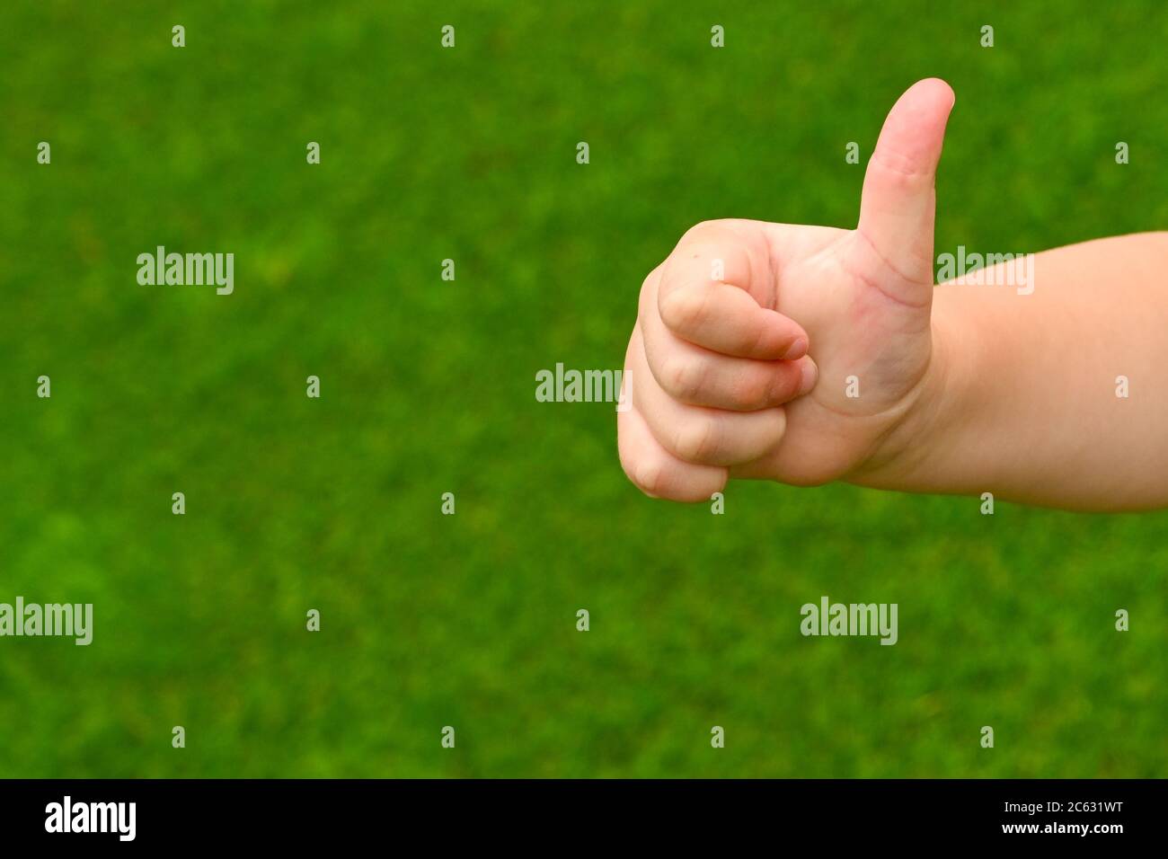 Thumbs up sign from a young person against a plain green background. Copy space. Stock Photo