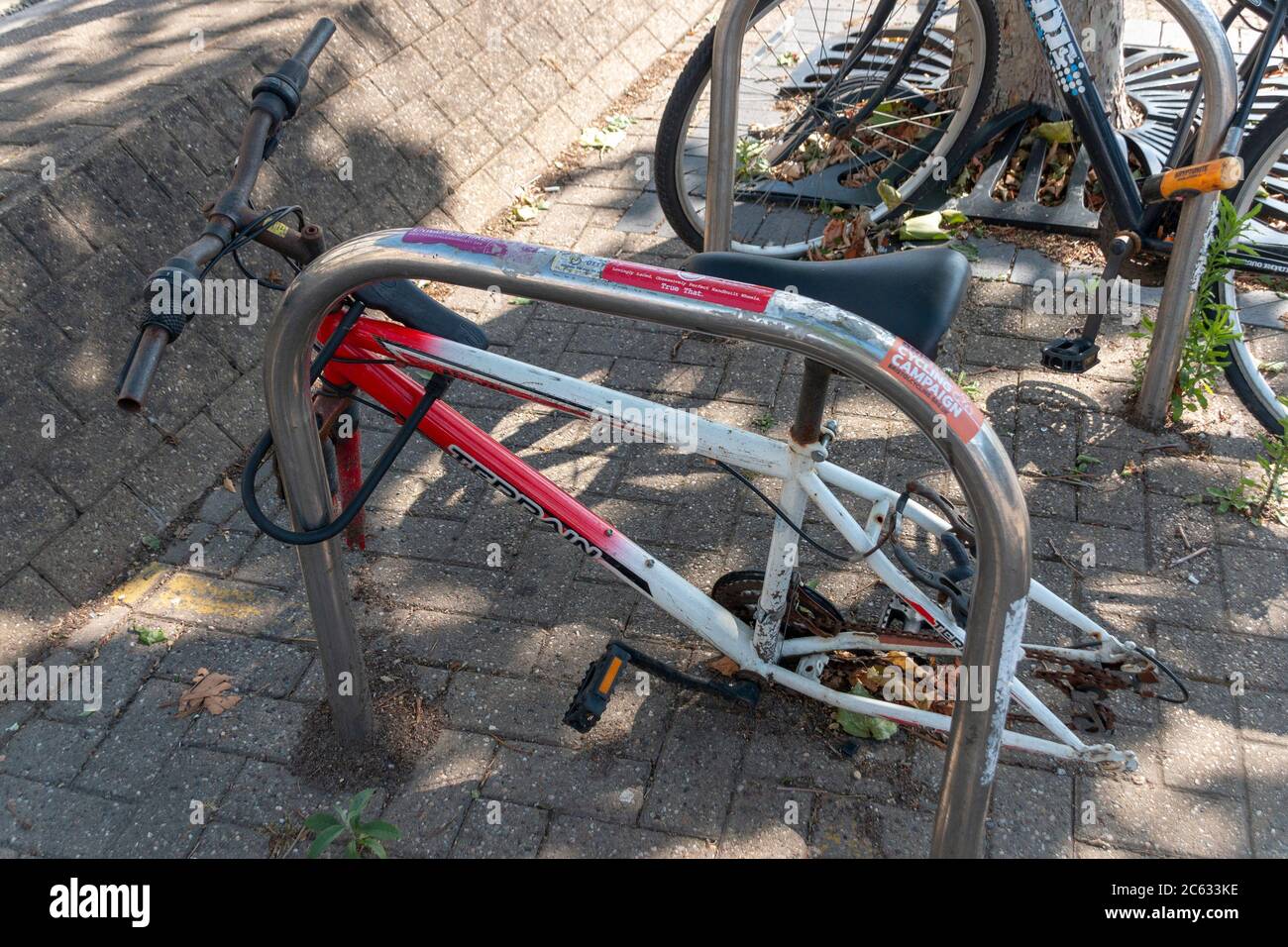 Bristol-June-2020-England-a close up view of a rusted old bicycle that has been abandoned and locked to a bike rake in the city where the wheels have Stock Photo