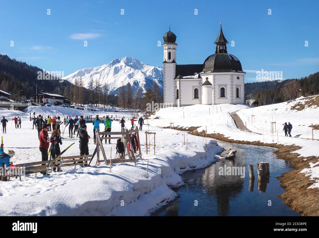 Seefeld, Tirol, Austria - 8 March 2020: Cross-country skiers on sunny track along a river and a pitoresque church Stock Photo