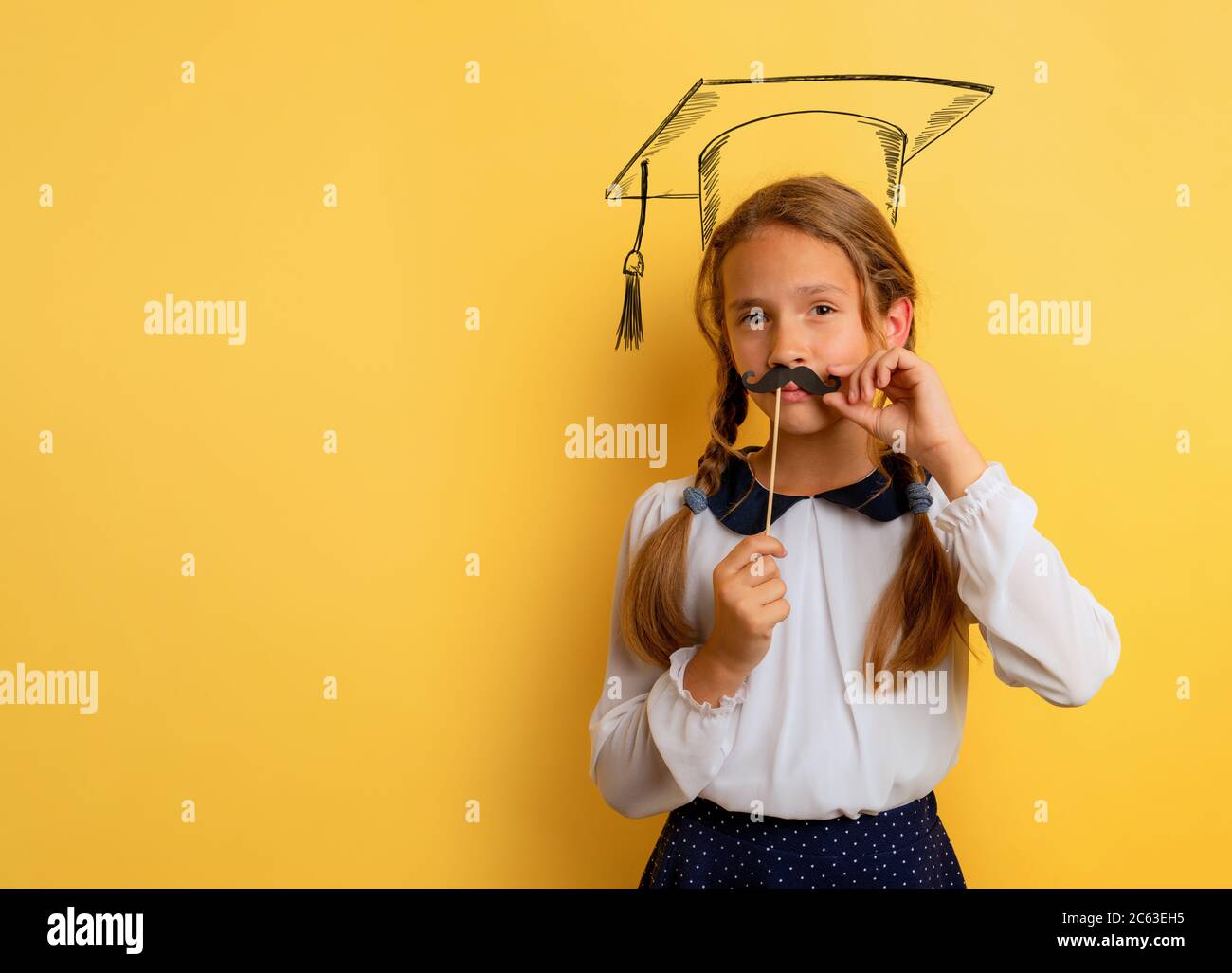 Young student acts like a graduate. Yellow studio background Stock Photo