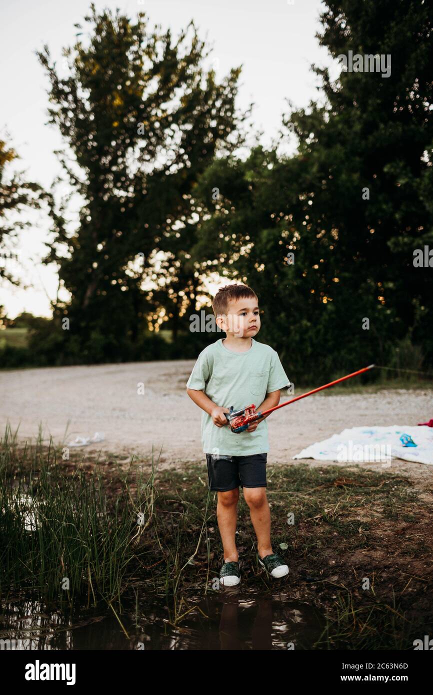 Young boy standing outside at lake holding fishing pole Stock Photo