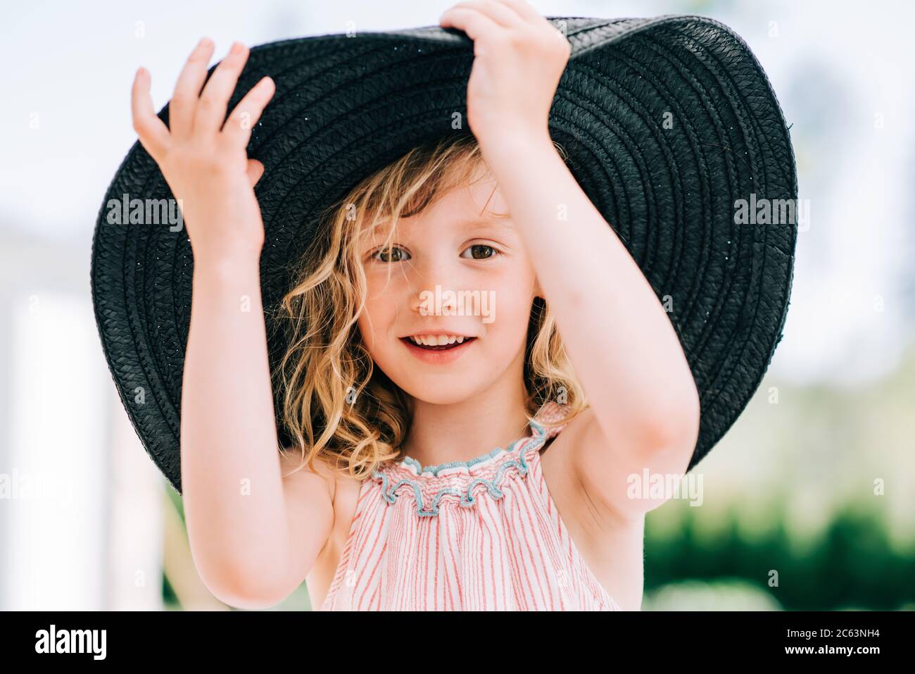 Candid portrait of a young girl laughing playing with a large sun hat