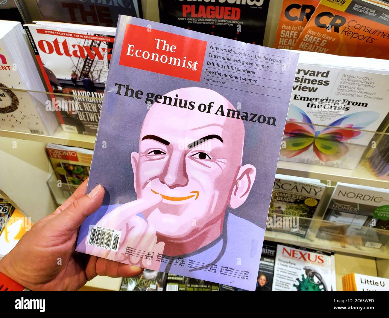 Montreal, Canada - June 30, 2020: The genius of Amazon title and a picture of Jeff Bezos as the Dr Evil on The Economist newspaper in a hand over a st Stock Photo