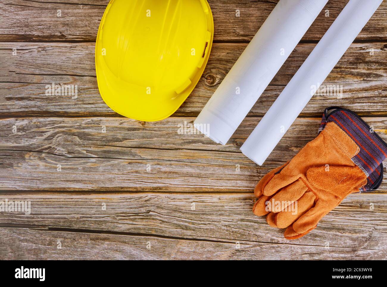 Builder of architects blueprints working on engineering office construction plans safety gloves on yellow safety helmet hard hat Stock Photo