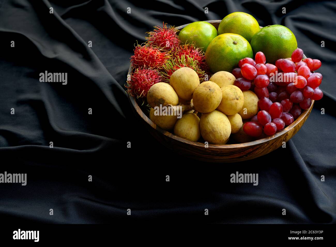 Many Thai fruits are put together in a wooden bowl on a black wrinkled