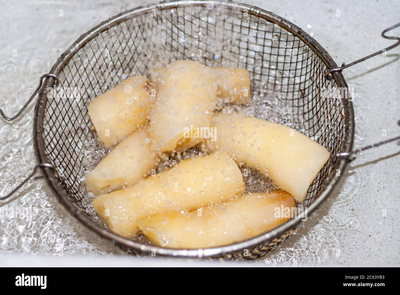 washing cassava with water in a metal strainer, Manihot esculenta. Cassava, also called mandioca, yuca, balinghoy, mogo, mandioca, kamoteng kahoy, tap Stock Photo