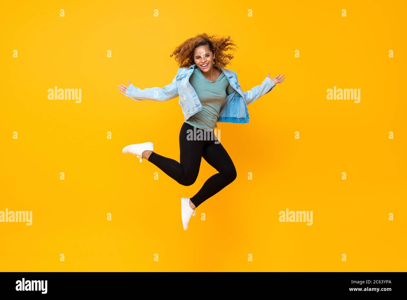 Happy energetic smiling young African-American woman jumping isolated on yellow background Stock Photo
