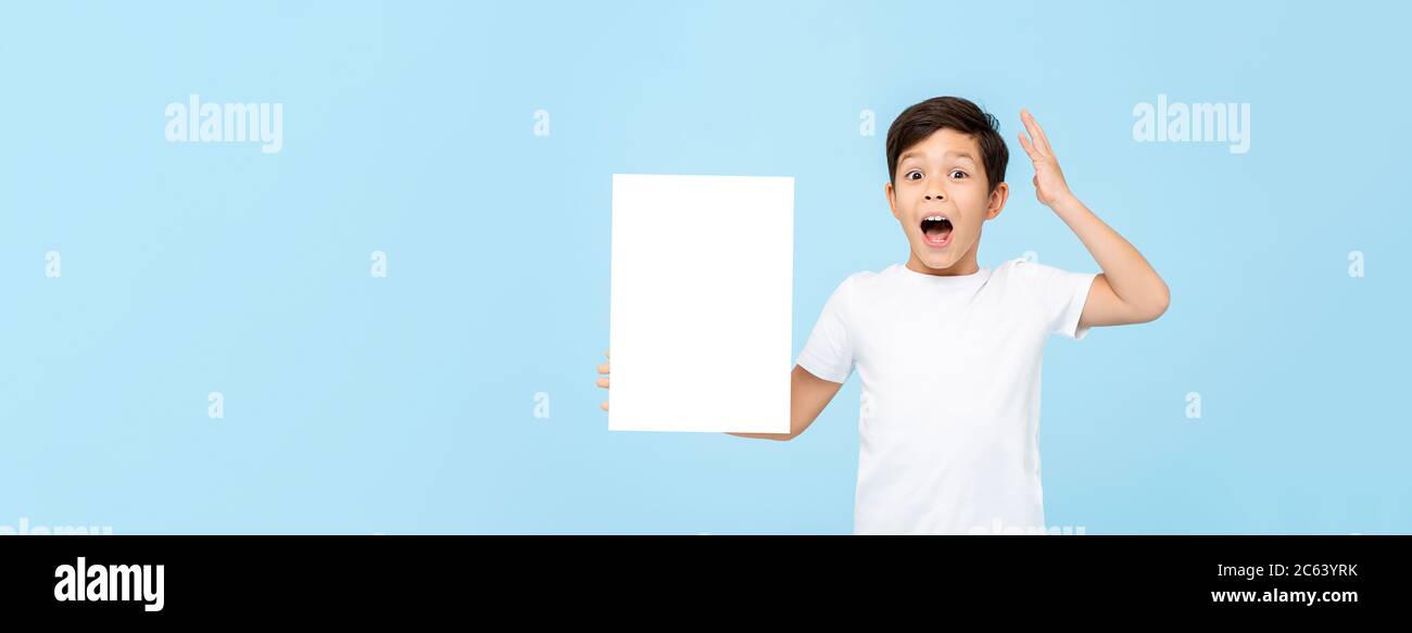 Cute little boy holding empty paper being shocked and gasping on light blue isolated banner background with copy space Stock Photo