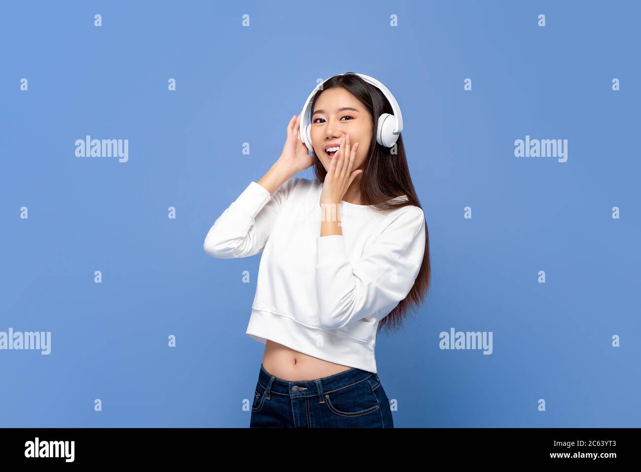 Young pretty Asian woman wearing wireless headphones listening to music isolated on light blue background Stock Photo