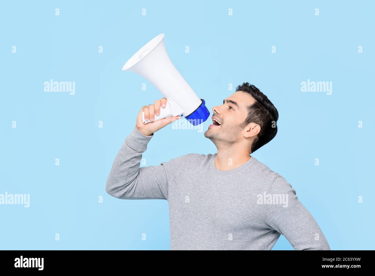 Caucasian man shouting on megaphone isolated on light blue background Stock Photo