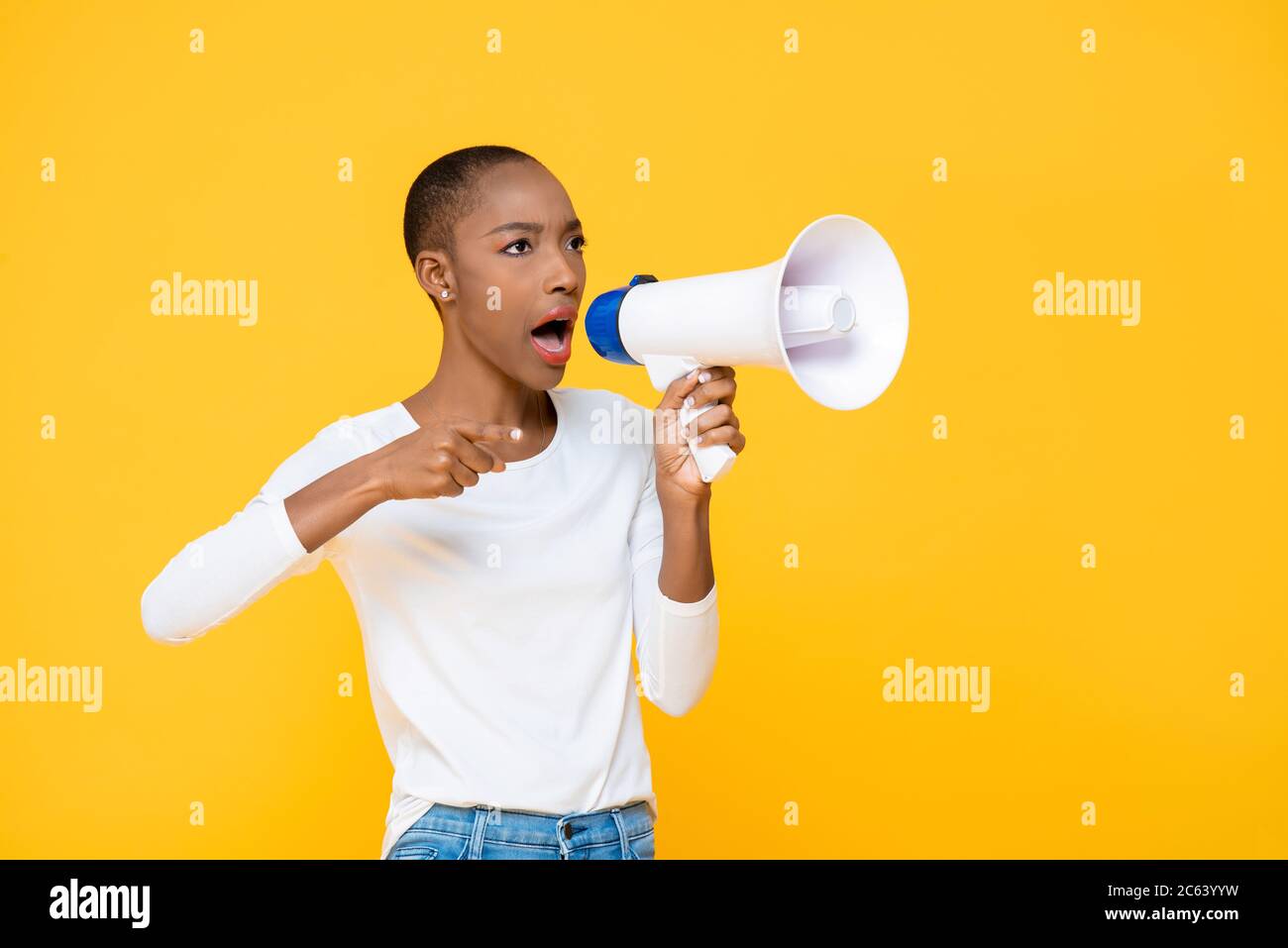 African American woman shouting on megaphone and pointing hand isolated on yellow background Stock Photo
