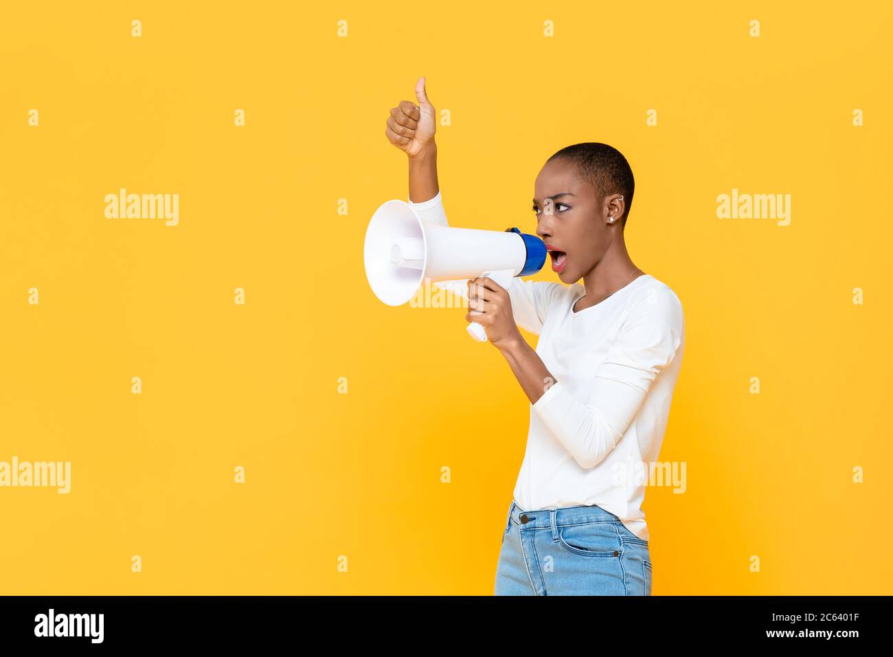 African American woman shouting on megaphone and giving thumbs up isolated on yellow background Stock Photo