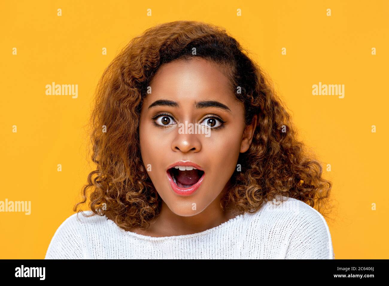 Surprised mixed African woman gasping isolated on yellow background Stock Photo