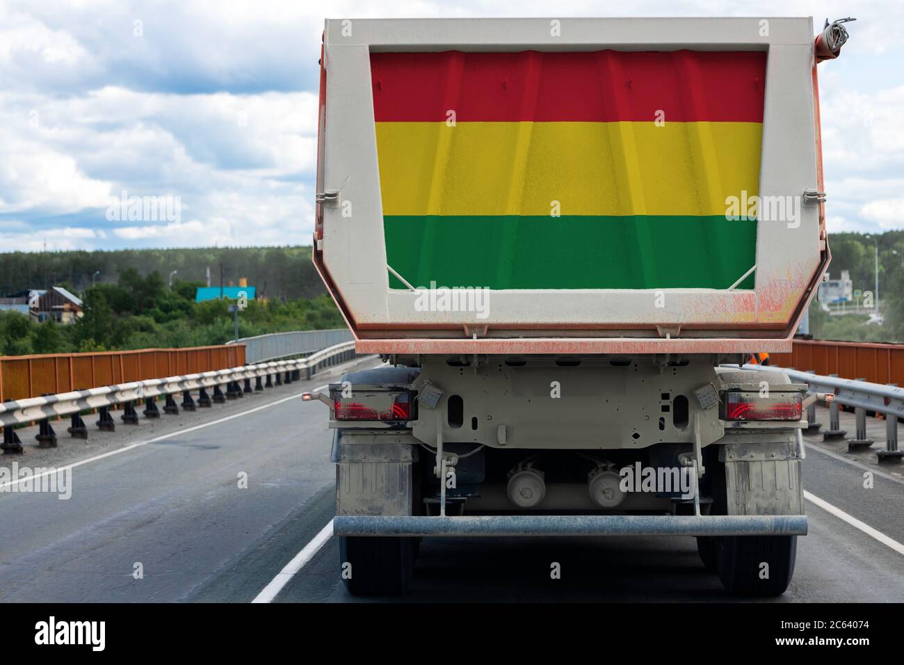 Big  truck with the national flag of  Bolivia  moving on the highway, against the background of the village and forest landscape. Concept of export-im Stock Photo