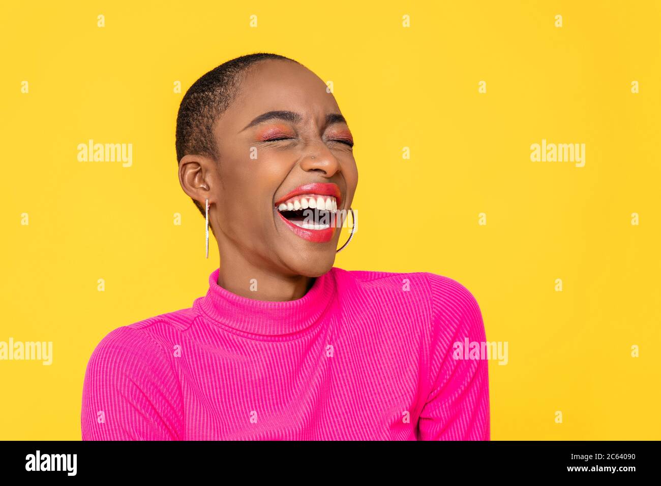 Happy optimistic African American woman in colorful pink clothes laughing isolated on yellow background Stock Photo