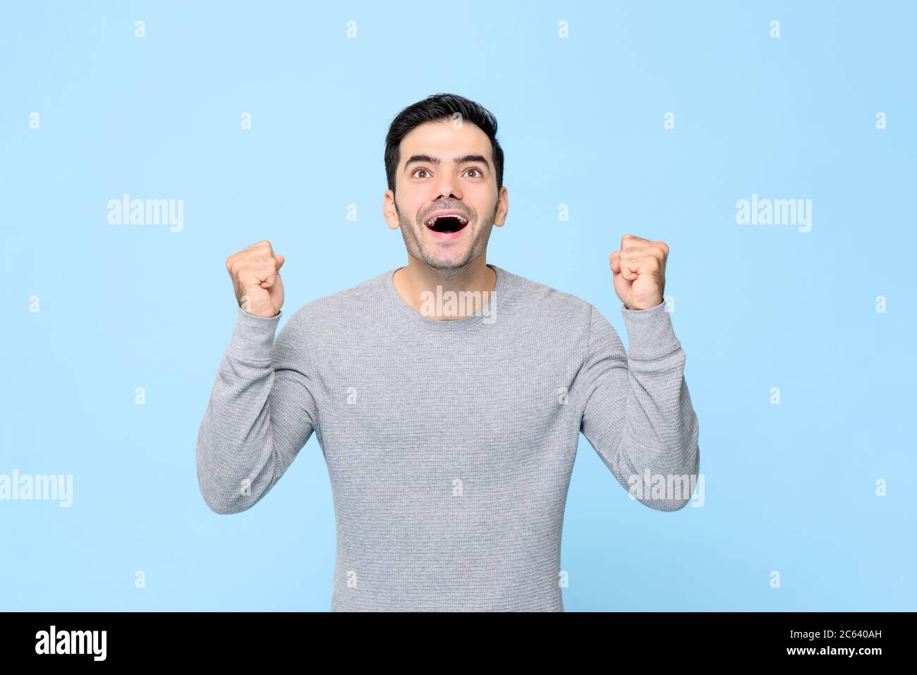 Excited surprised Caucasian man clenching his fists and looking up isolated on light blue background Stock Photo